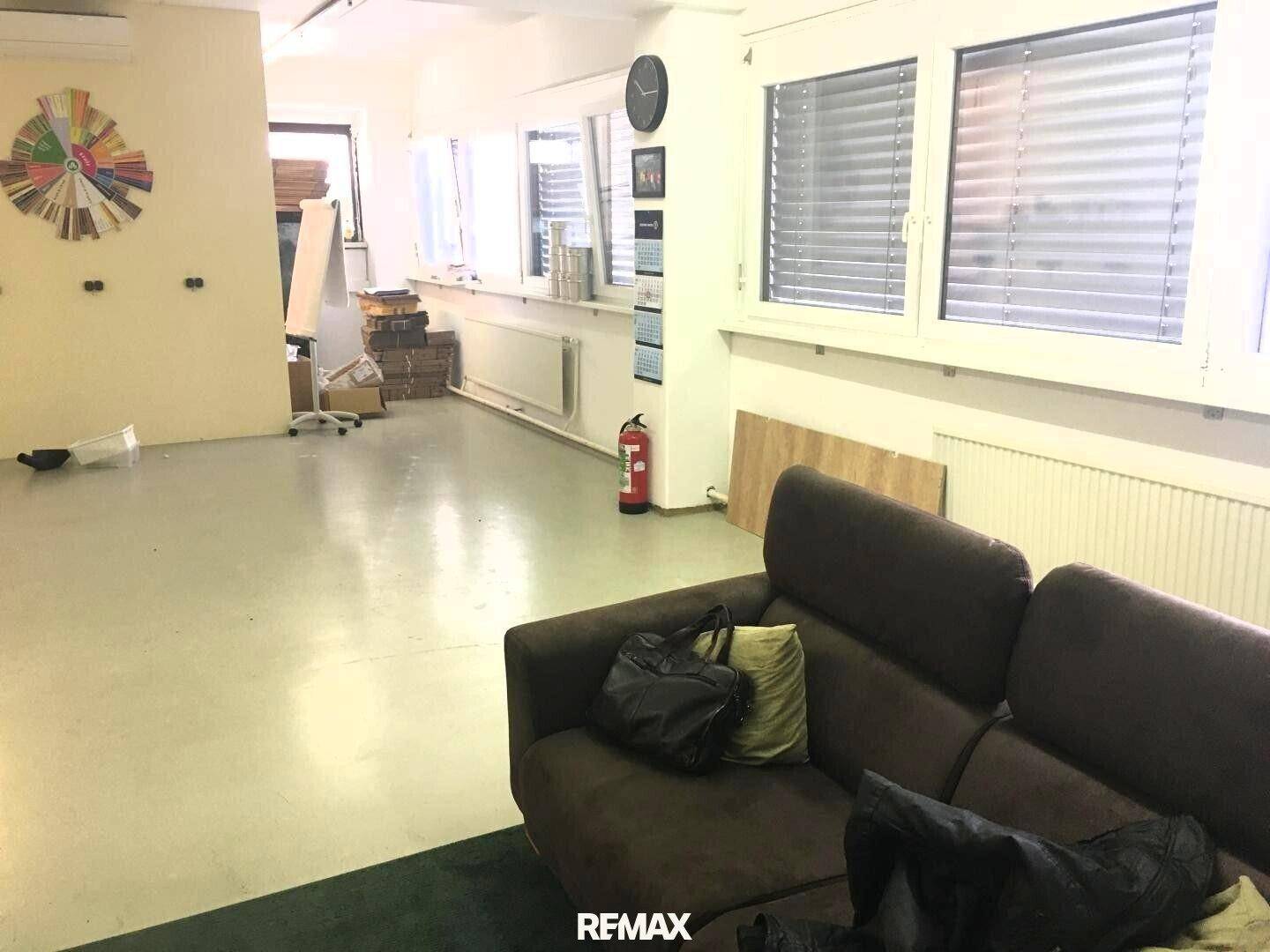 Geräumiger Büroraum mit großen Fenstern, Jalousien und einem Sofa, bereit zur individuellen Gestaltung.
