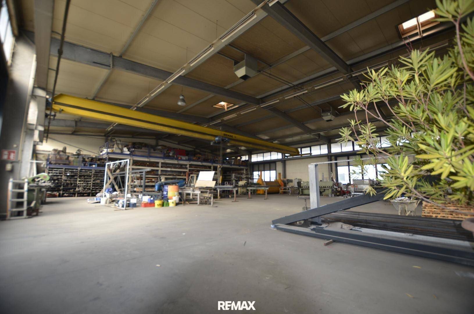 Geräumige Industriehalle mit hoher Decke, sichtbaren Stahlträgern und einem gelben Kran, ideal für Lagerung oder Produktion.