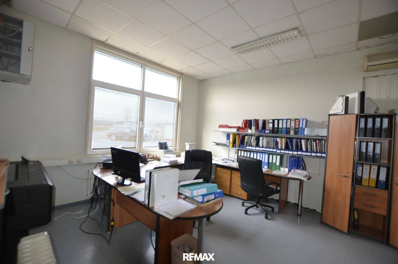 Helles Büro mit zwei Arbeitsplätzen, Aktenschränken und einem großen Fenster, das viel Tageslicht hereinlässt.