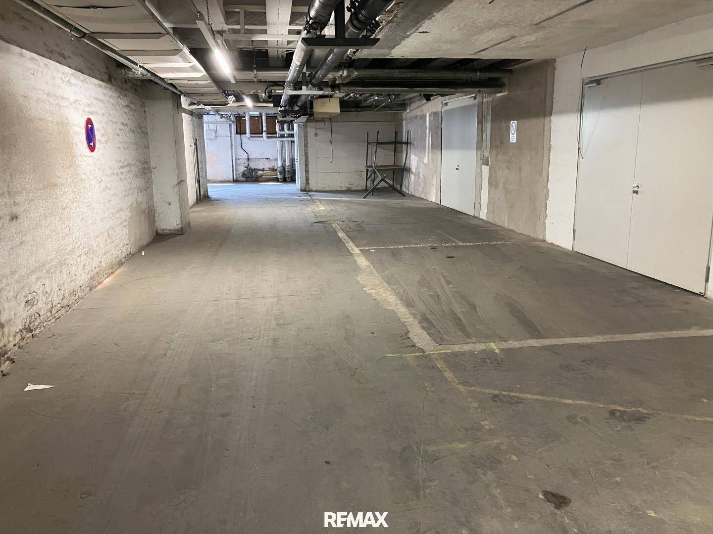 Weitläufige Tiefgarage mit Betonwänden, sichtbaren Rohren und ausreichend Platz für mehrere Fahrzeuge.