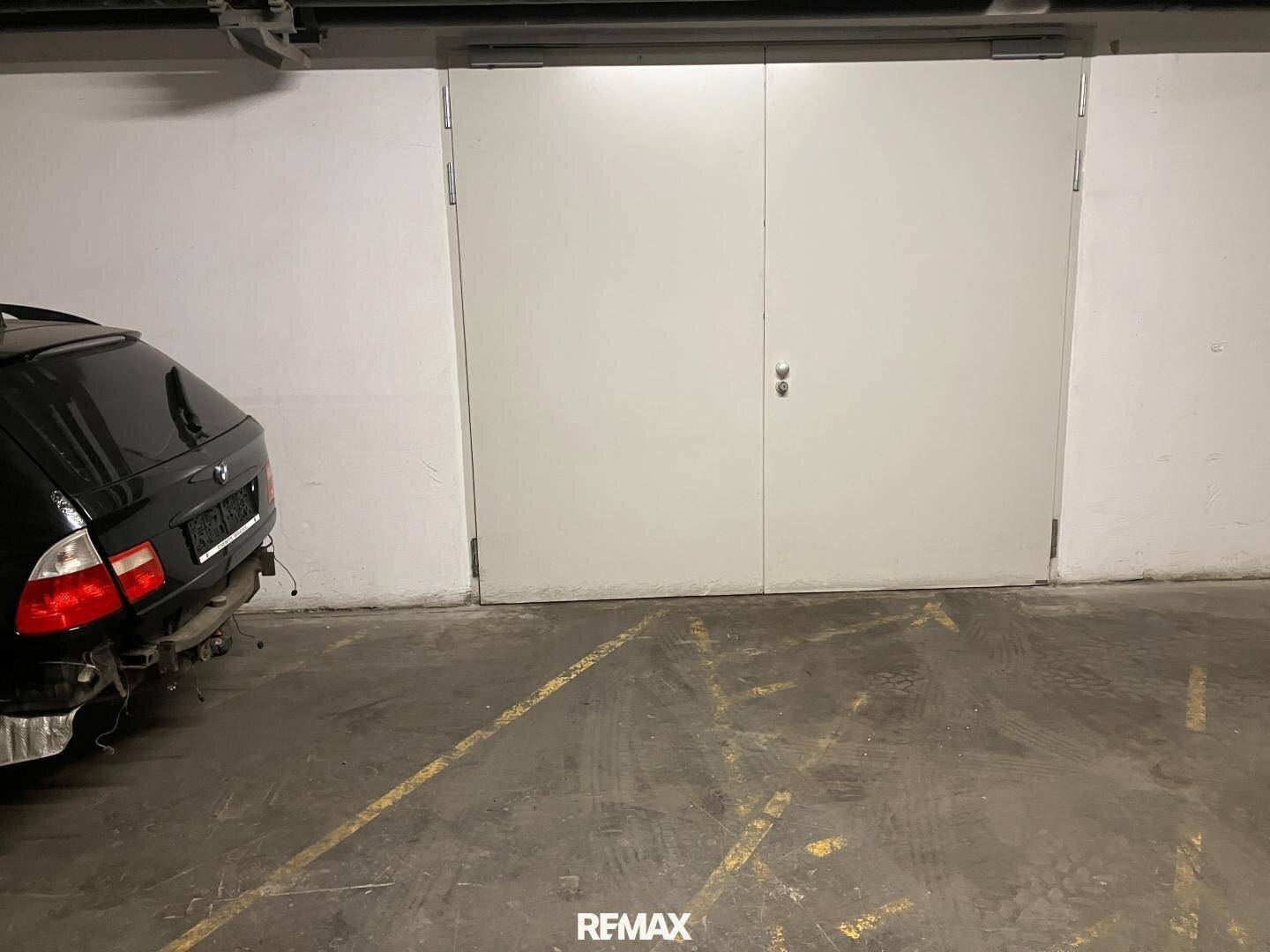 Tiefgaragenstellplatz mit weißen Türen und einem Betonboden, daneben ein geparktes Fahrzeug.