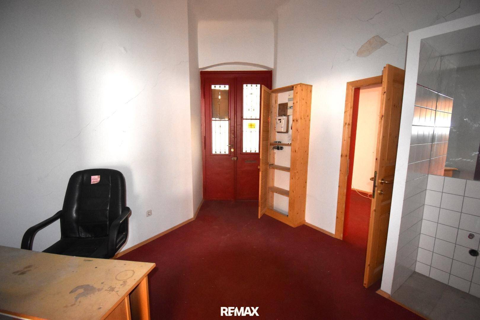 Büroähnlicher Raum mit rotem Teppichboden, Holztüren und einem Zählerschrank.