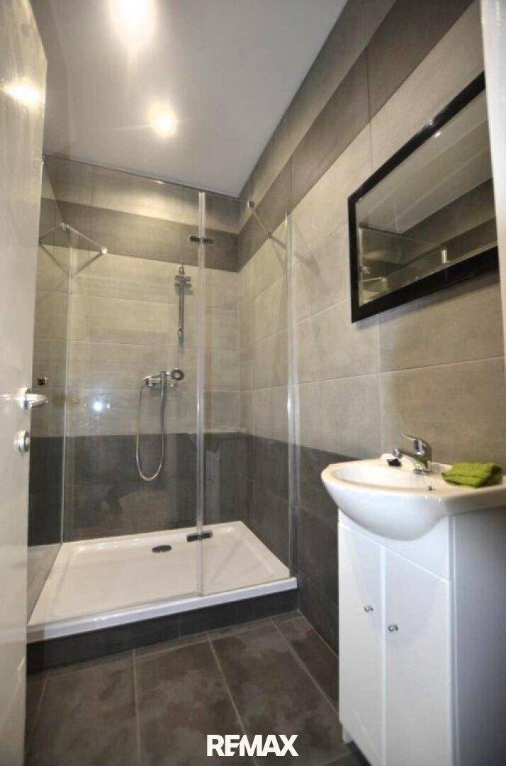 Modernes Badezimmer mit grauen Fliesen, Duschkabine und einem einzelnen Waschbecken.