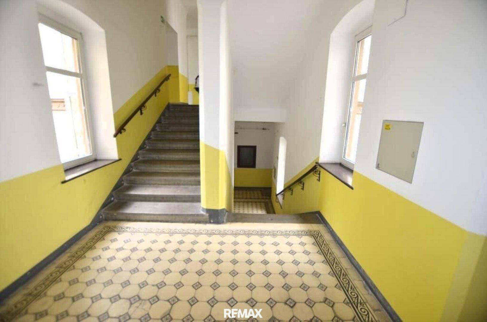 Historisches Treppenhaus mit gelb gestrichenen Wänden und gemusterten Fliesenböden.