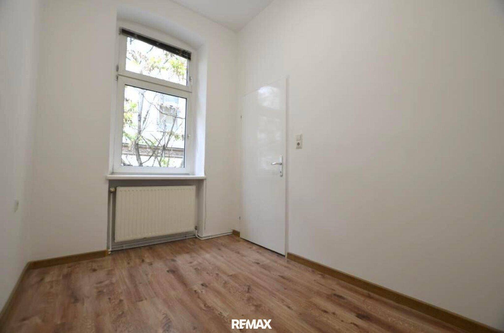 Kleines, helles Zimmer mit Laminatboden, weiß gestrichenen Wänden und einem Fenster.