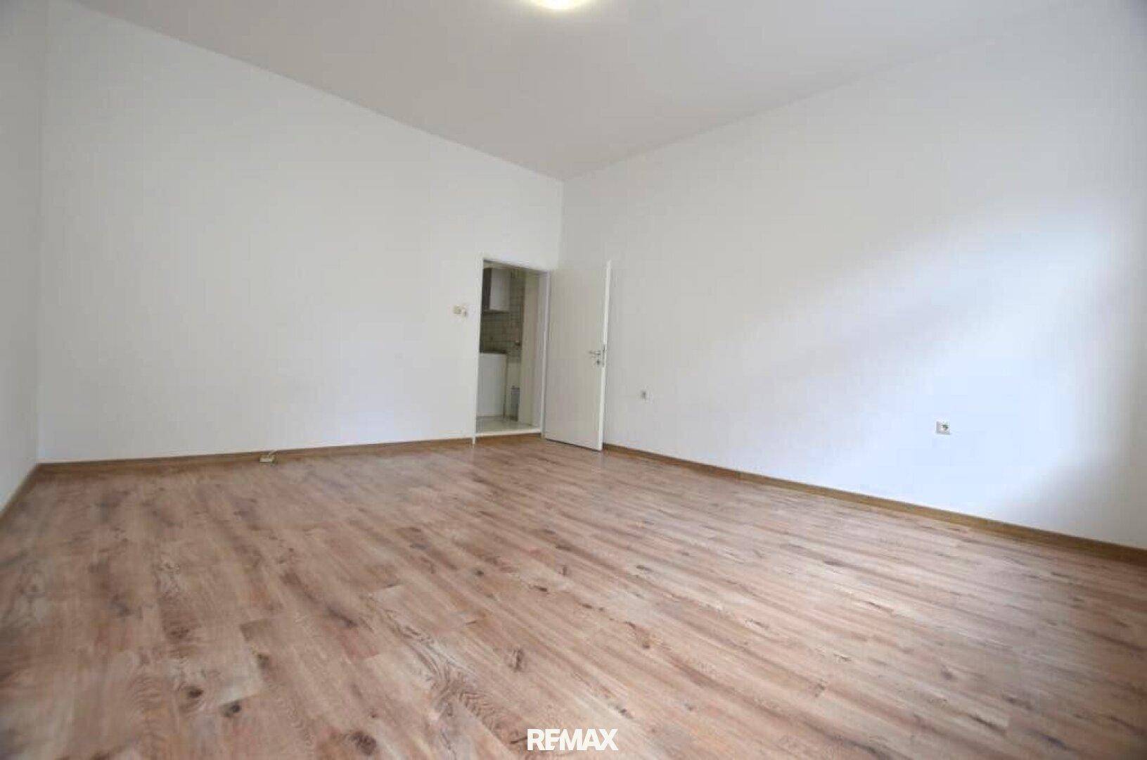 Heller, leerer Raum mit Laminatboden und weißen Wänden, bereit zur individuellen Gestaltung.