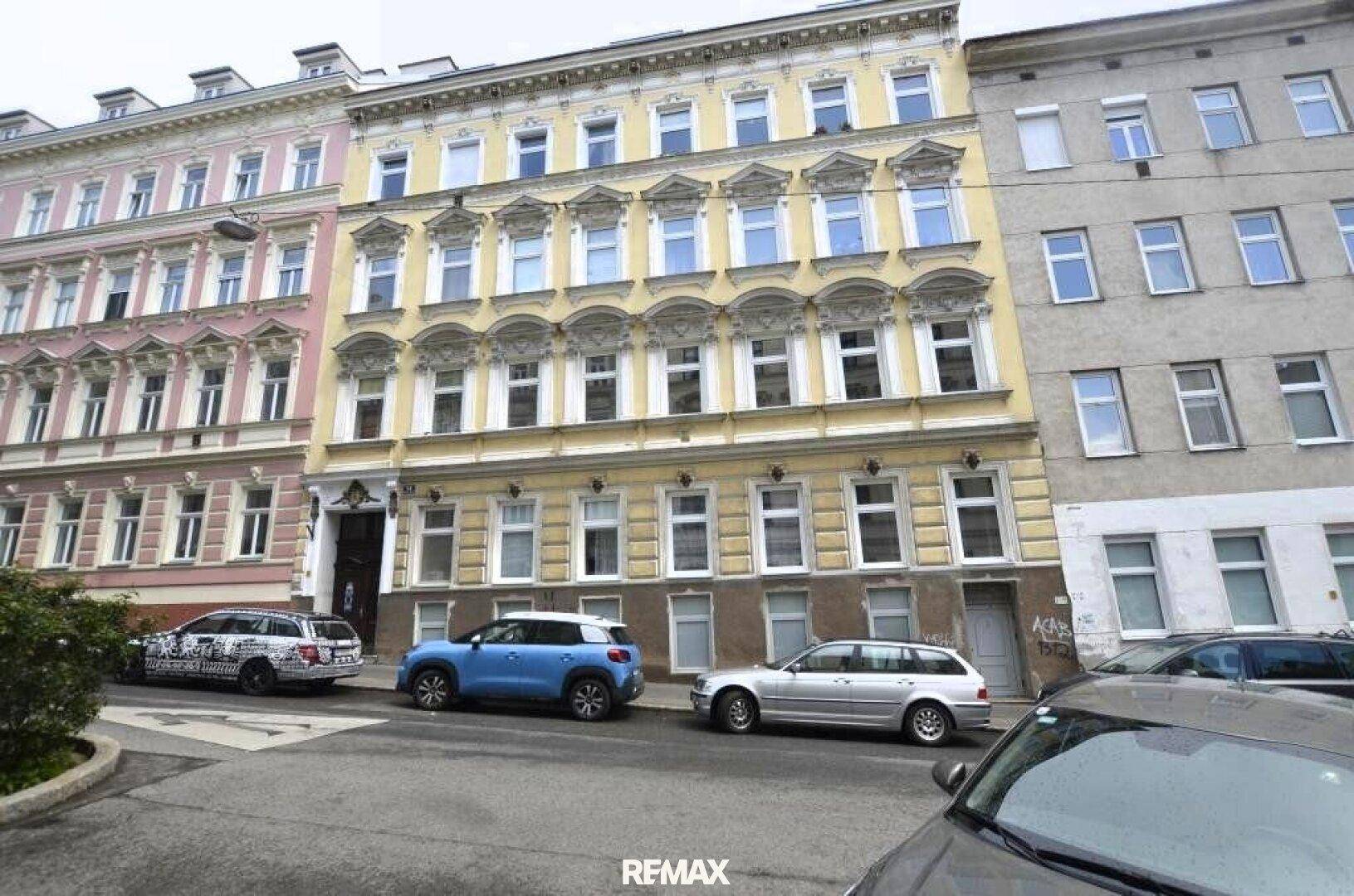 Historisches Mehrfamilienhaus mit klassischer Fassade und parkenden Autos auf der Straße.