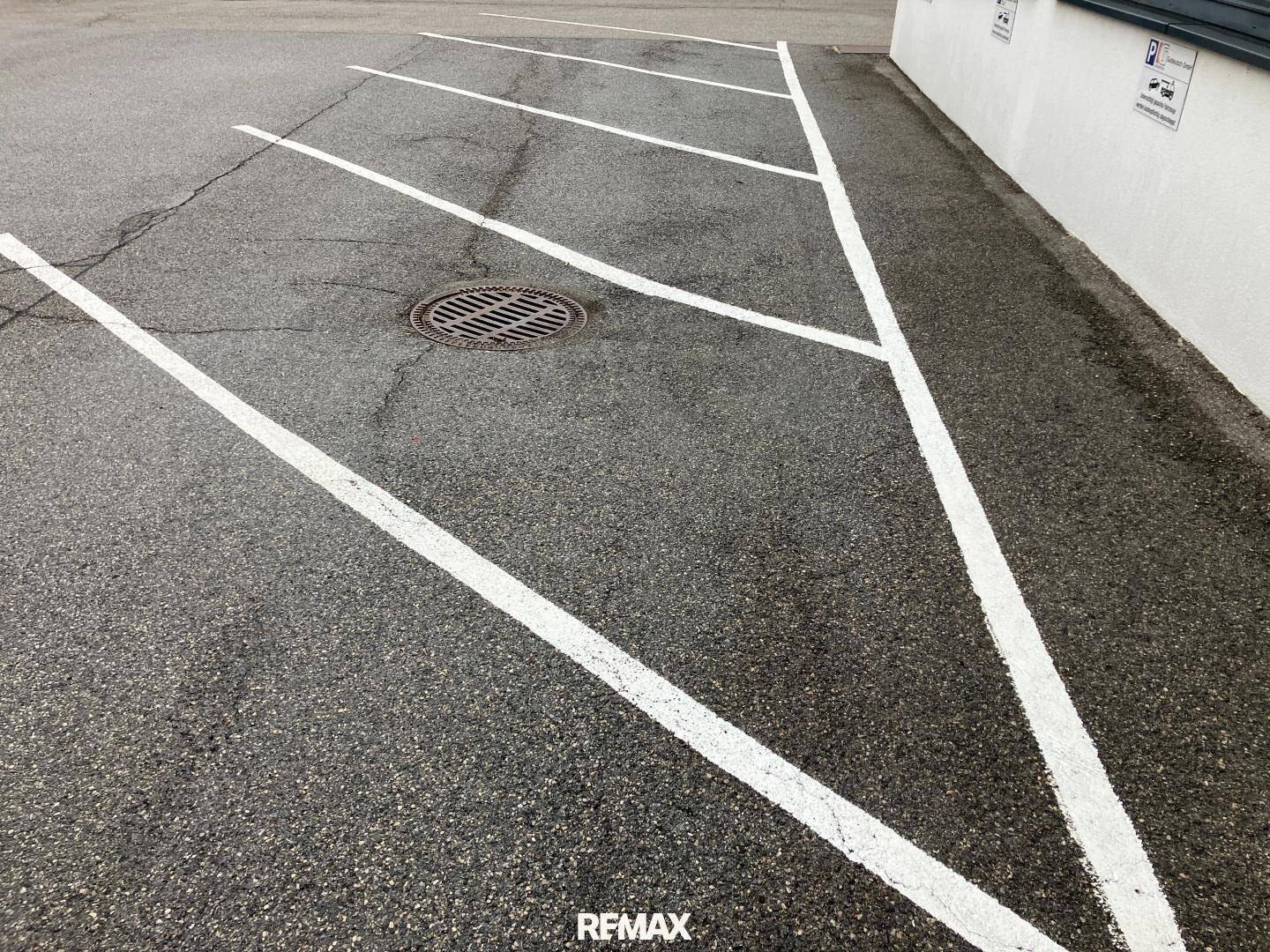 Parkplatz mit markierten Stellflächen und einem Gullydeckel auf dem Asphaltboden.