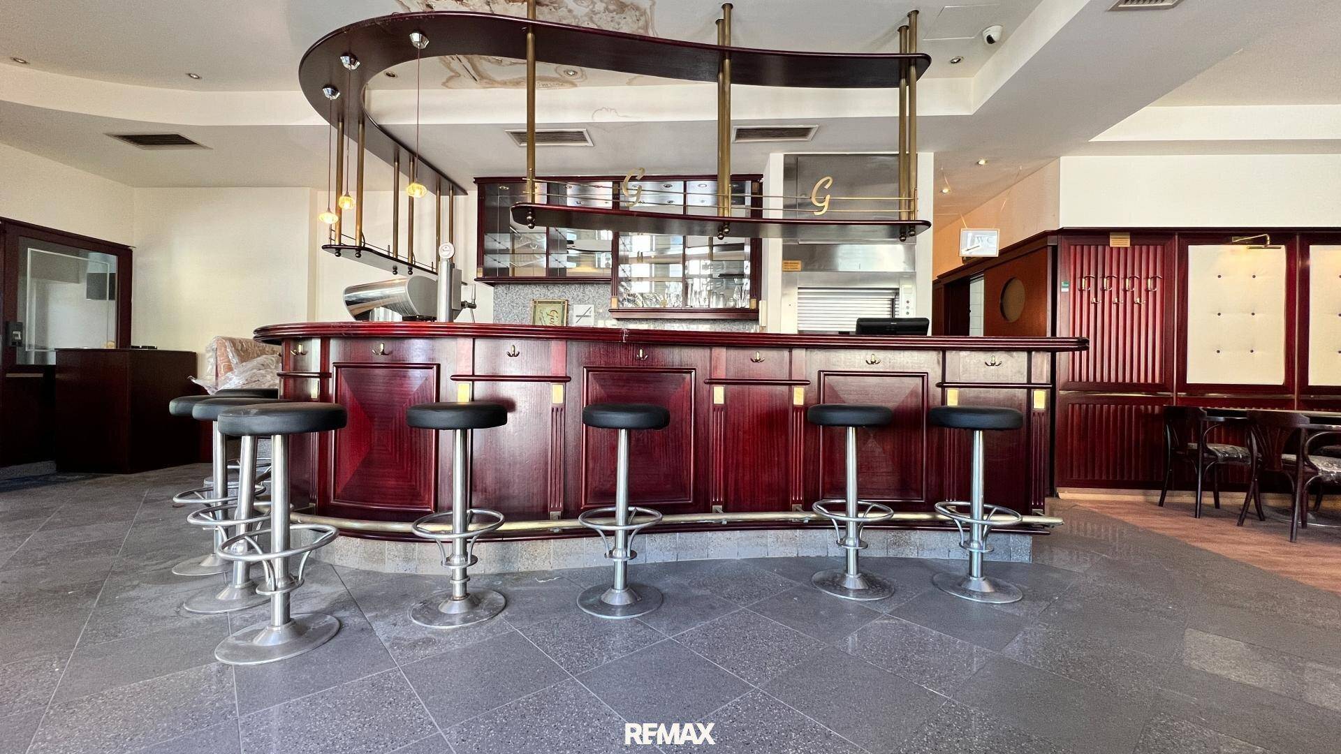 Elegante Bar mit dunklem Holz, Barhockern und gefliestem Boden in einem Gastronomiebetrieb.