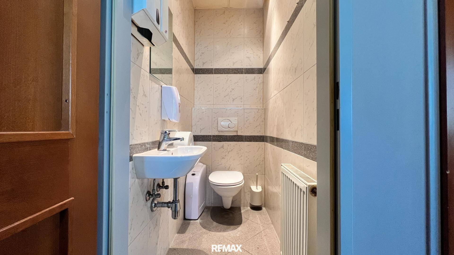 Kleiner Toilettenraum mit Wand-WC, Waschbecken und Fliesen an Wänden und Boden.