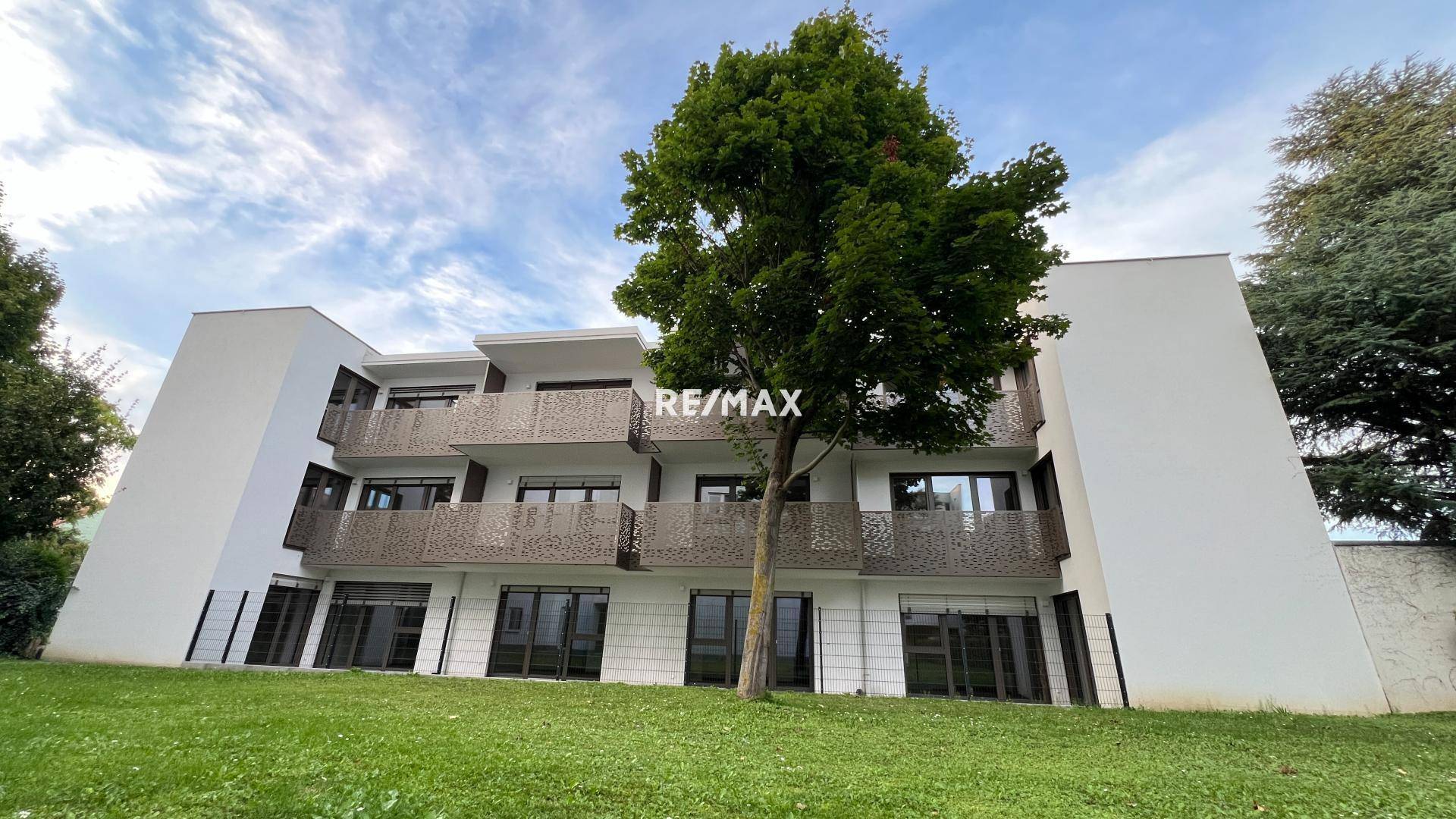 Moderne Wohnanlage mit mehreren Balkonen und einer gepflegten Grünfläche sowie Bäumen im Vordergrund.