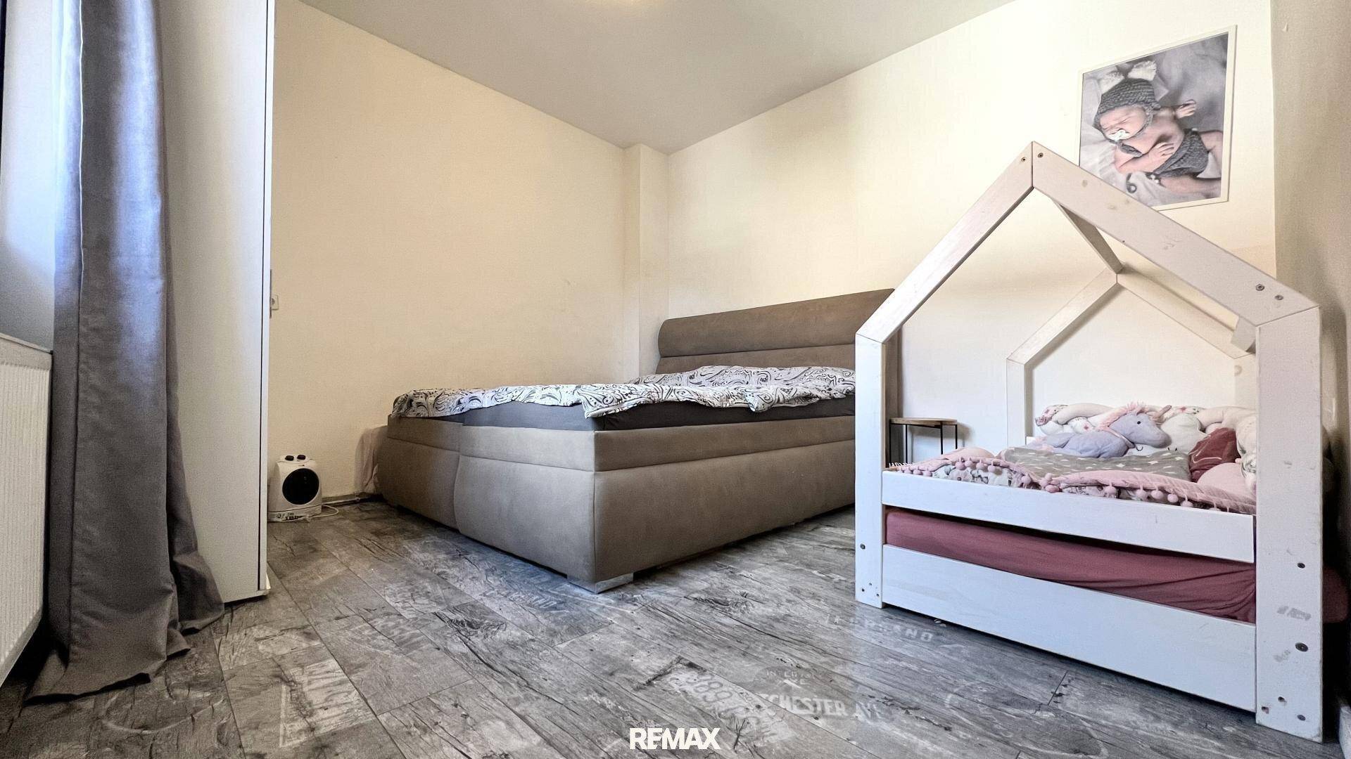 Helles Schlafzimmer mit einem Doppelbett und einem Kinderbett, ausgestattet mit Laminatboden.