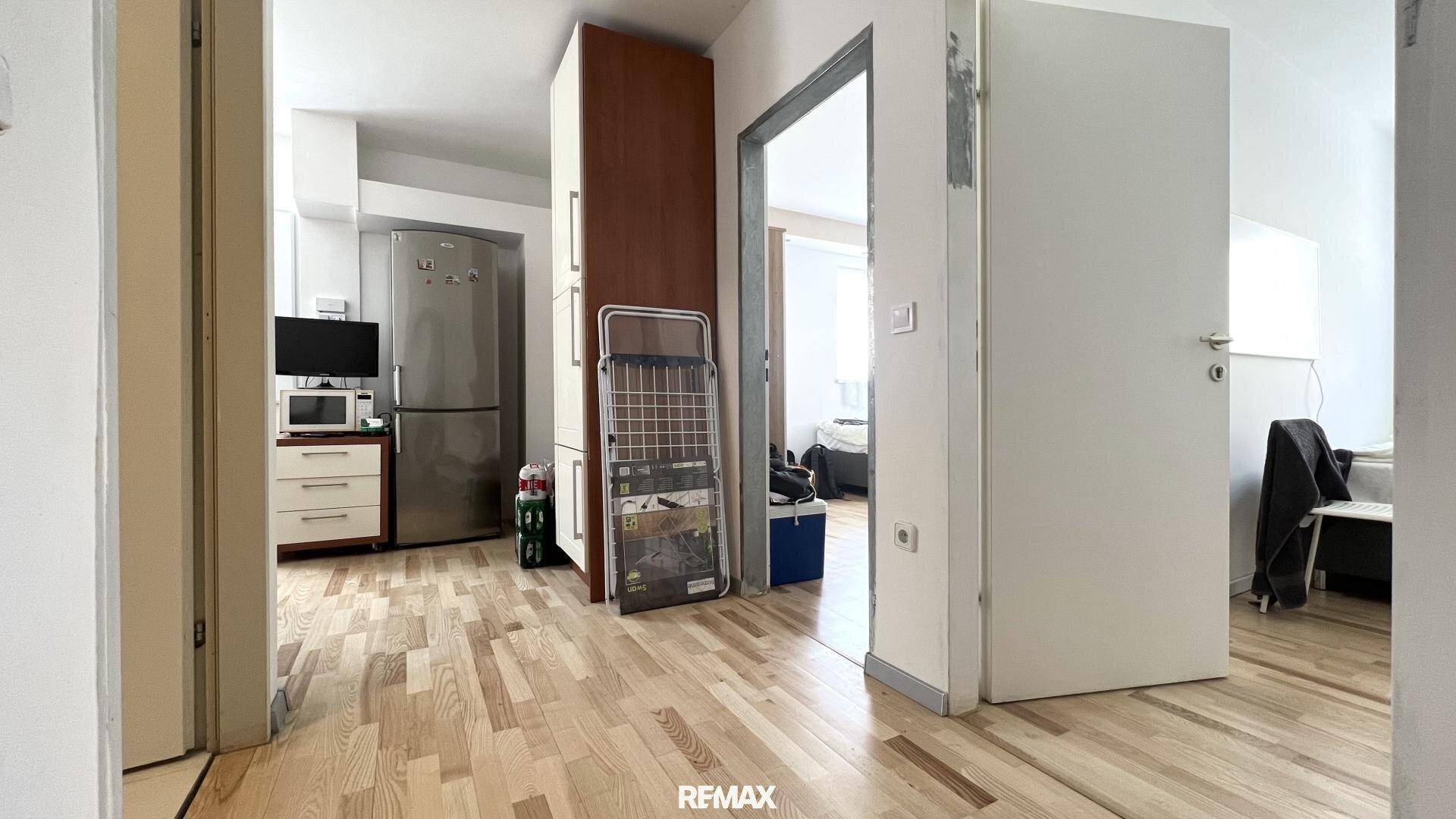 Heller Flur mit Holzfußboden, Kühlschrank und offenen Türen zu angrenzenden Wohnbereichen.