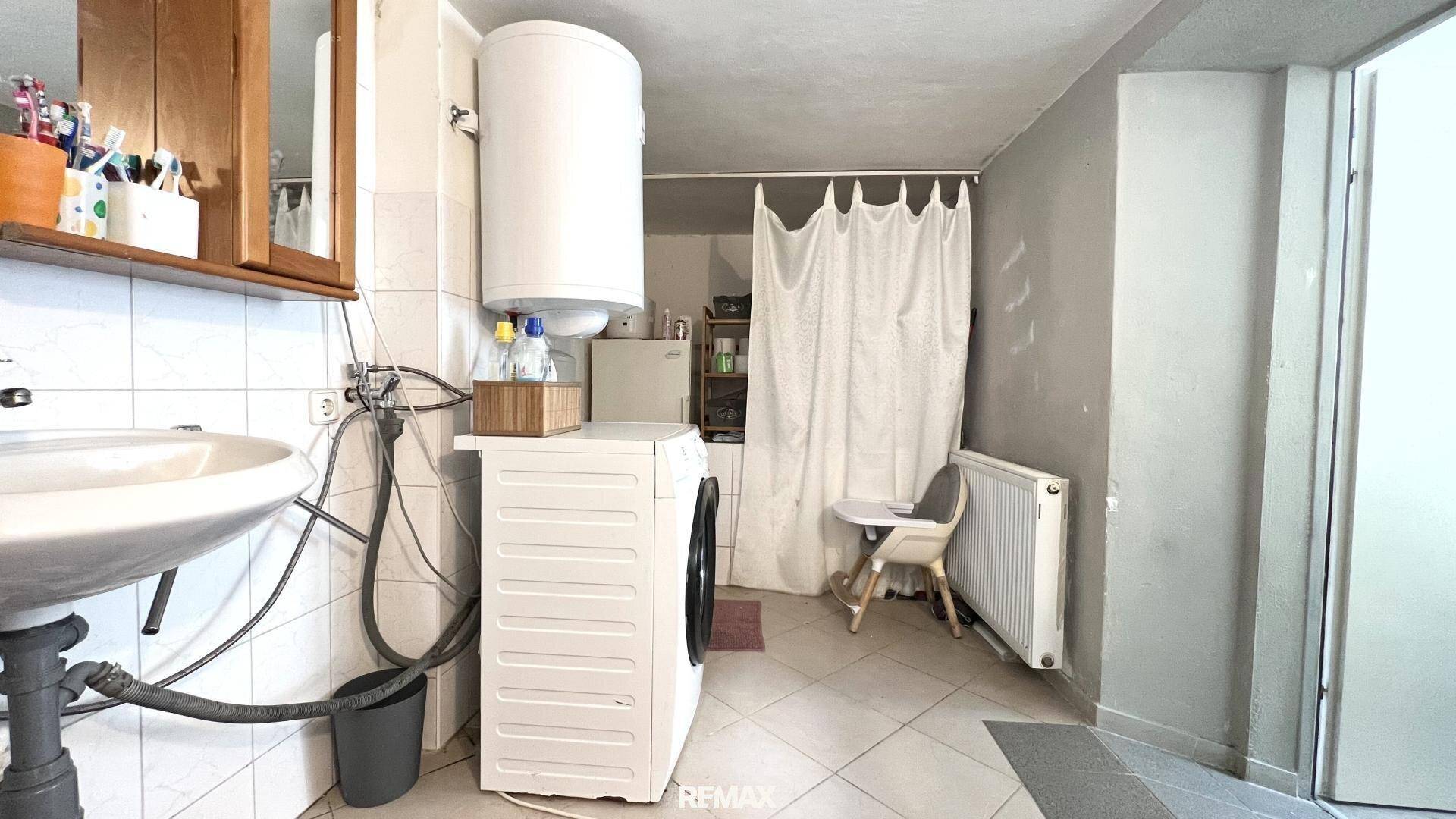 Praktisches Badezimmer mit Waschbecken, Waschmaschine, Warmwasserboiler und Duschbereich.