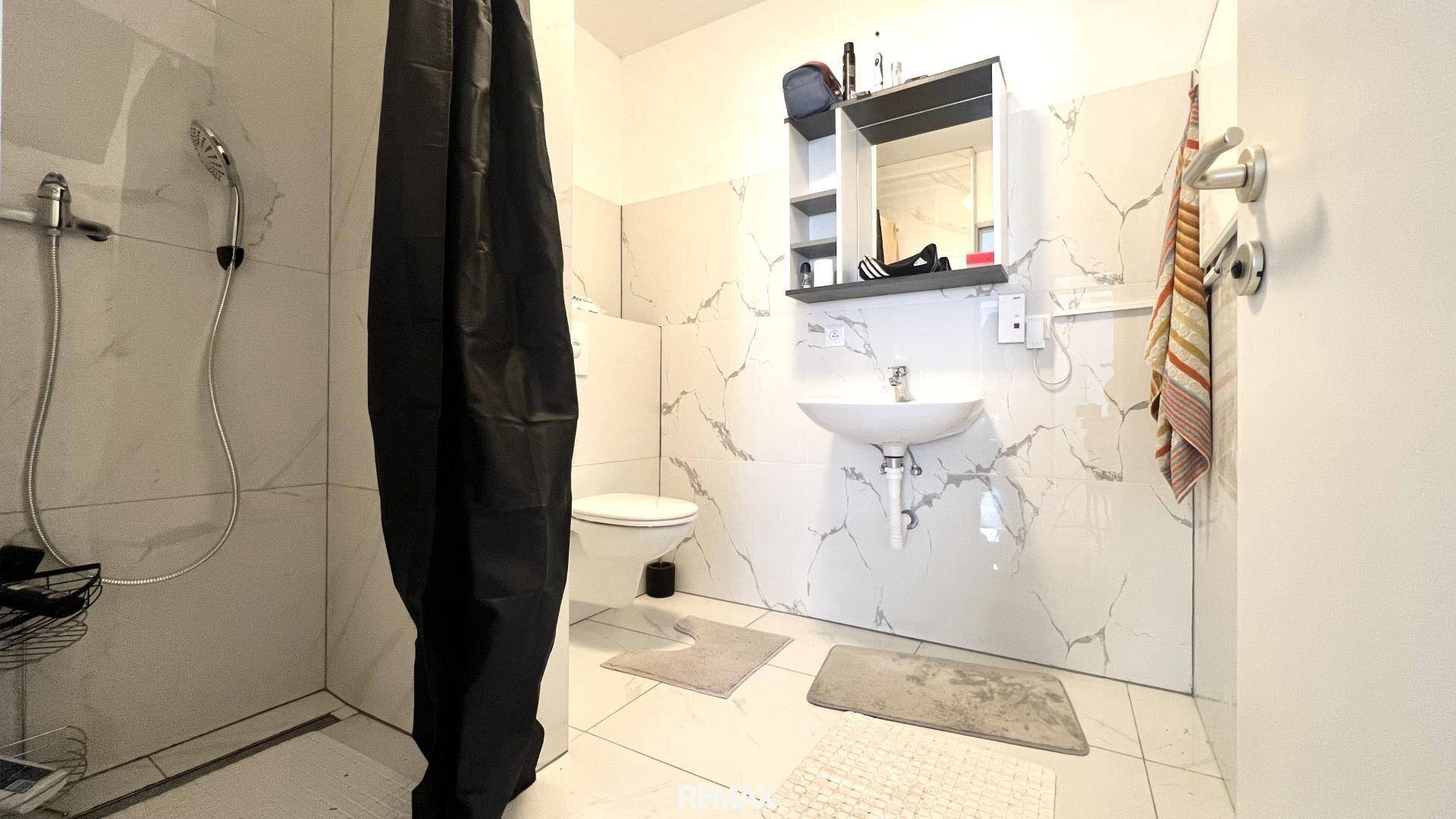 Modernes Badezimmer mit weißen Marmorfliesen, Dusche, Waschbecken und wandhängendem WC.