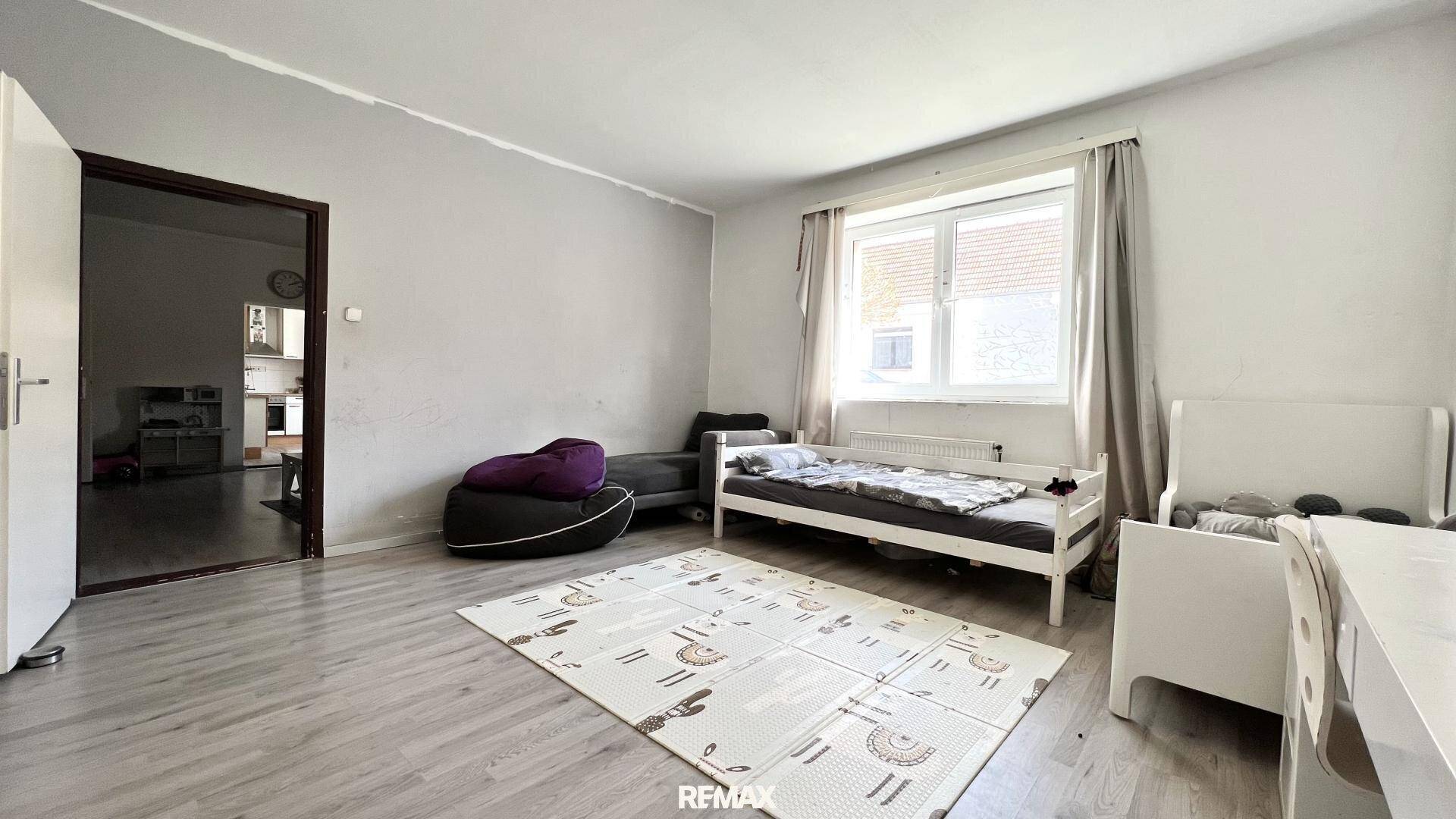 Helles Schlafzimmer mit Einzelbett, Spielmatte auf dem Boden und Zugang zu einem weiteren Raum.