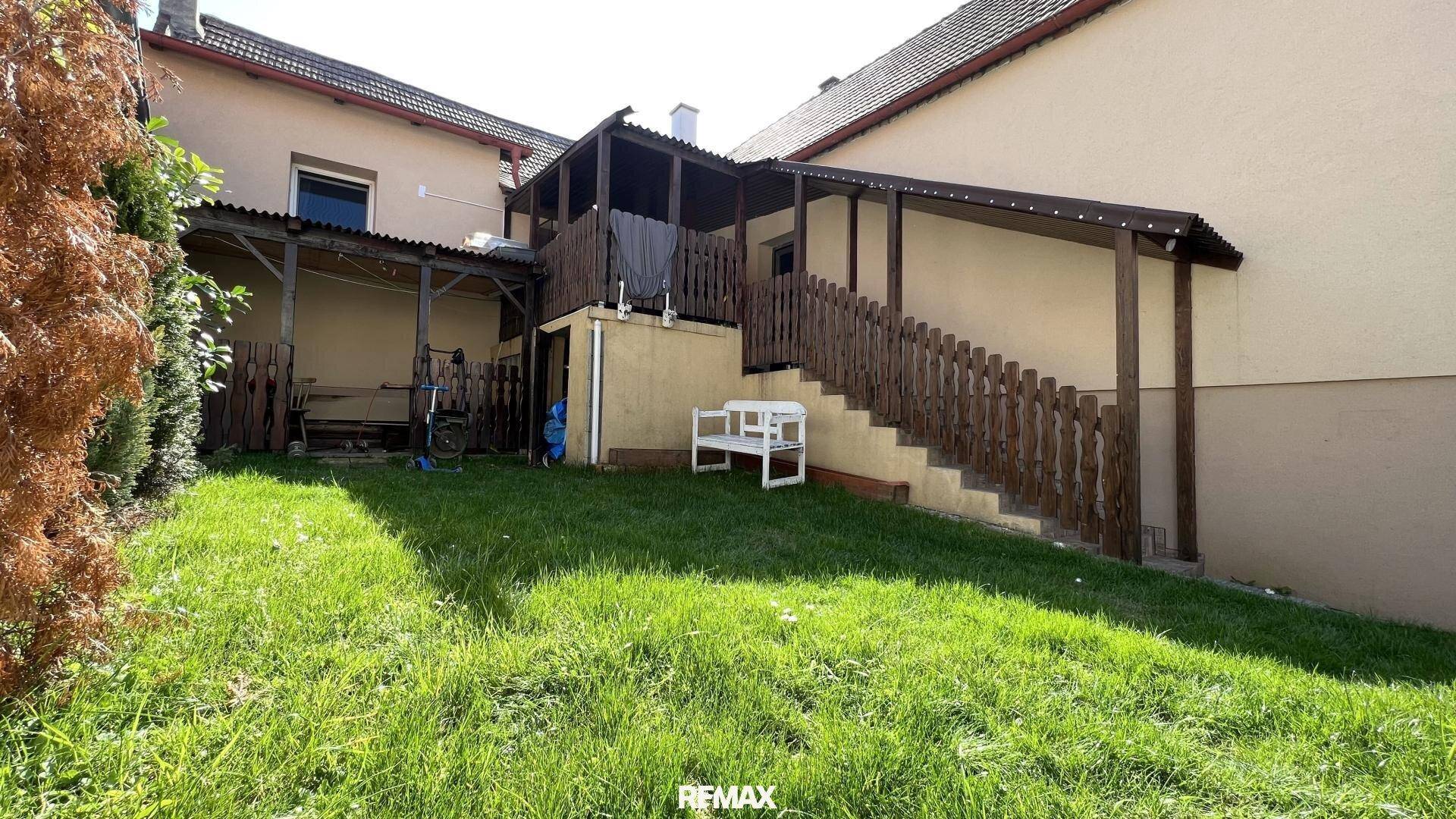 Grüner Gartenbereich mit überdachter Terrasse und Holztreppe, die zu einem oberen Bereich führt.