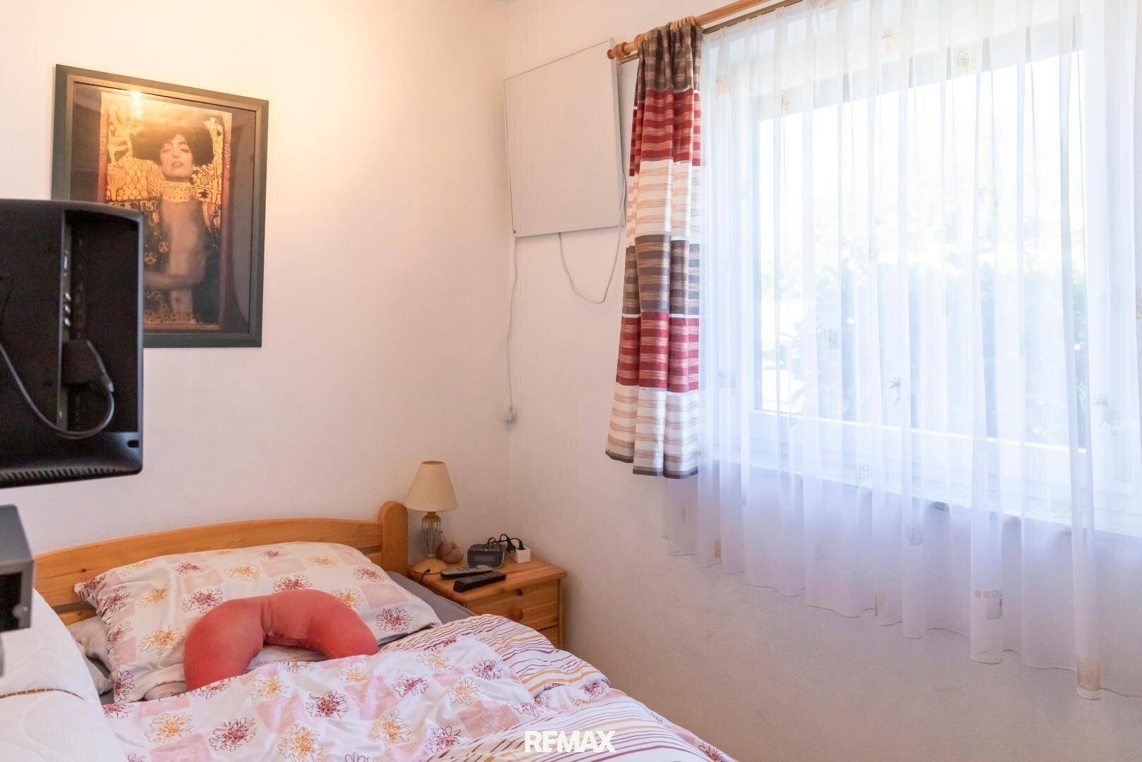 Gemütliches Schlafzimmer mit Einzelbett, Nachttisch und einem Fenster mit Vorhängen.