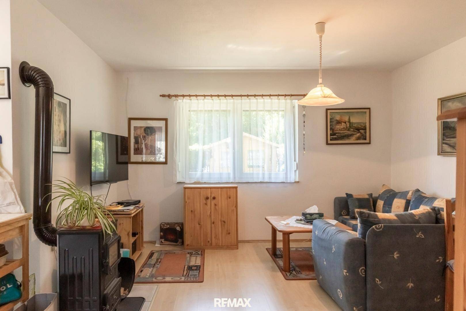 Gemütliches Wohnzimmer mit Holzofen, hellem Laminatboden und Blick in den Garten.