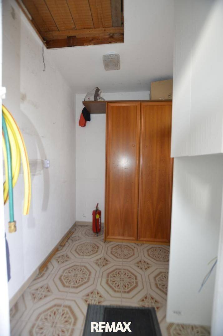 Kleiner Abstellraum mit gemusterten Fliesen, Holzschrank und sichtbarem Feuerlöscher.