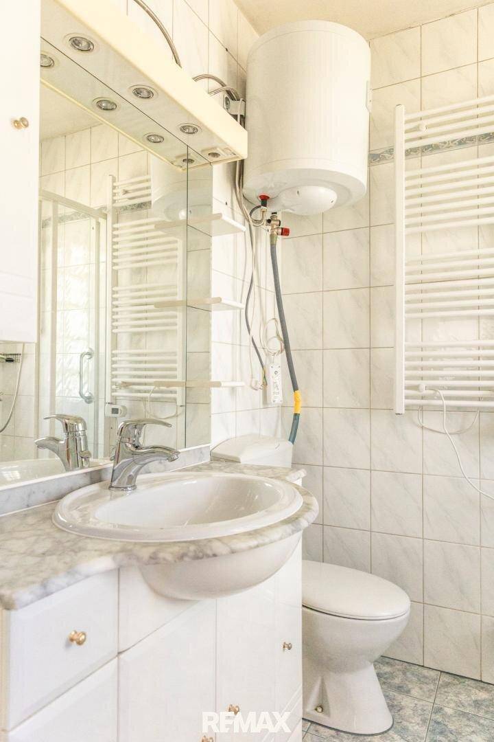 Helles Badezimmer mit weißen Fliesen, Marmorwaschtisch, Dusche und beheiztem Handtuchhalter.