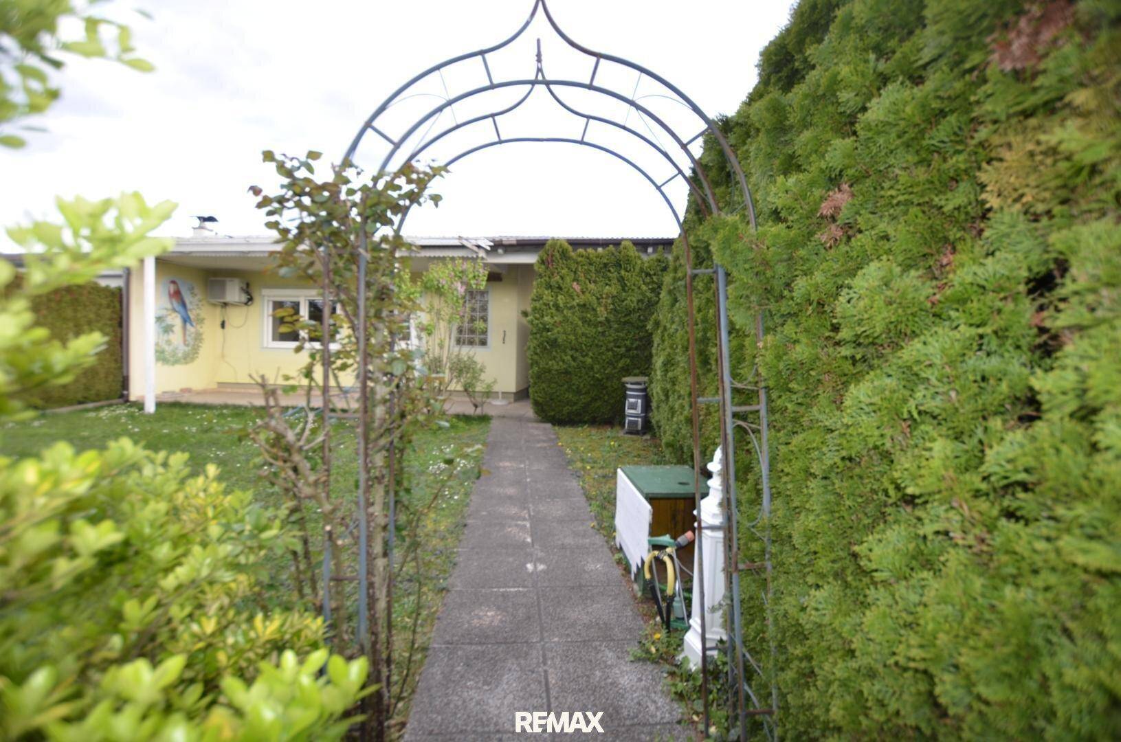 Gartenweg mit einem Rankbogen führt zum Haus, umgeben von hohen Hecken und Grünflächen.