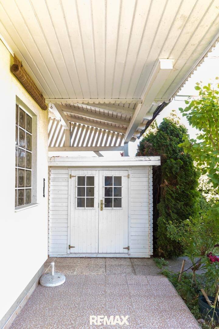 Kleiner weißer Gartenschuppen neben dem Haus mit überdachtem Terrassenbereich.