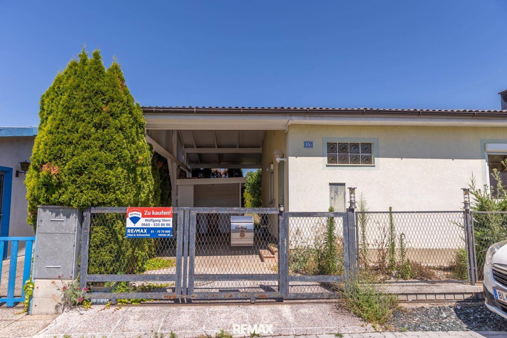 Eingangsbereich eines Hauses mit Metalltor, Verkaufsanzeige und überdachtem Stellplatz.