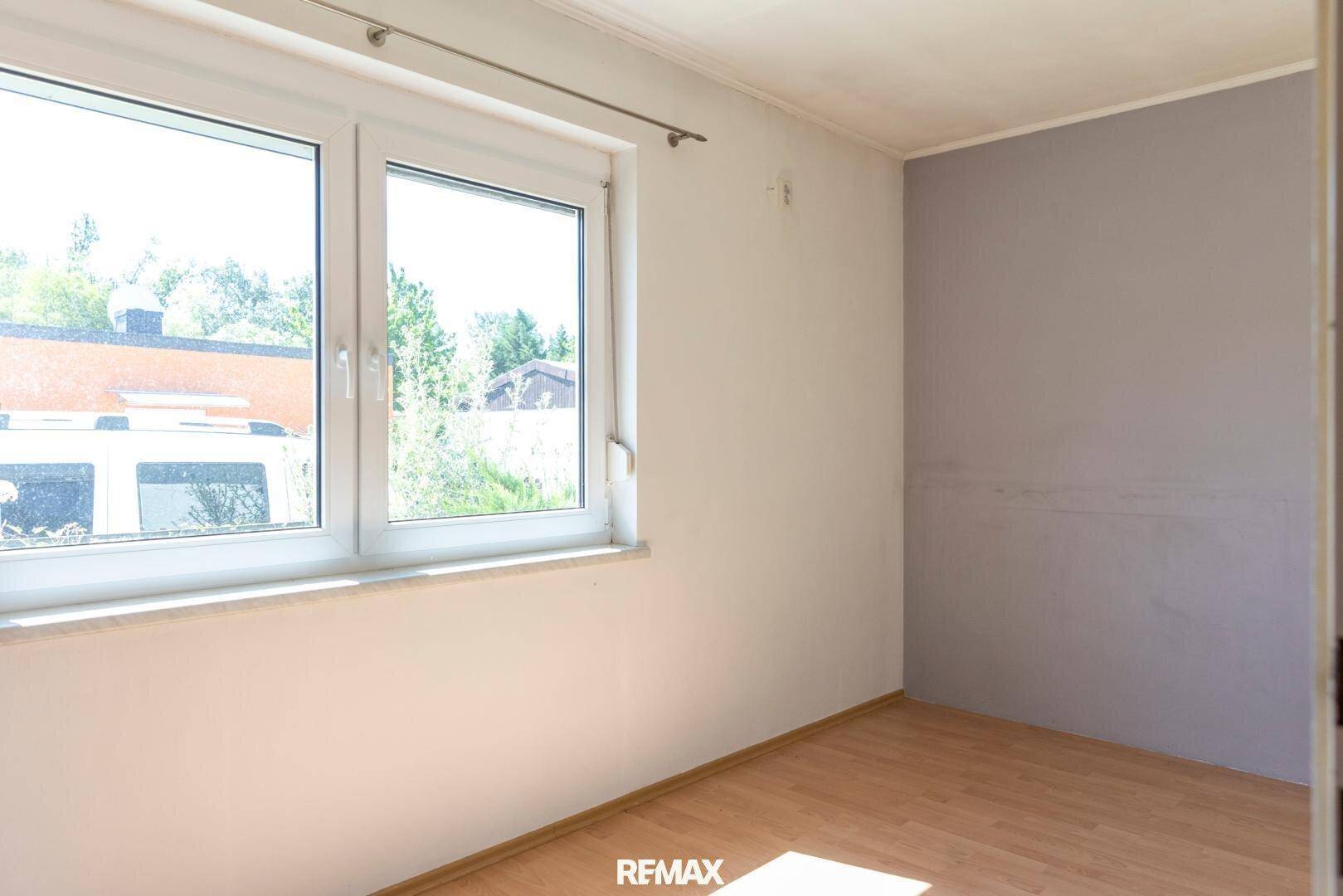 Leeres Schlafzimmer mit Holzboden und großem Fenster, das viel natürliches Licht hereinlässt.