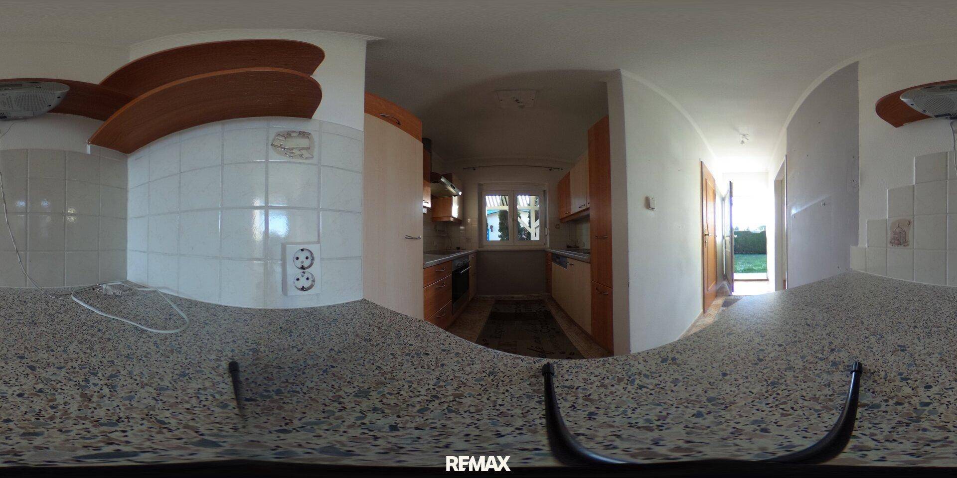 Panoramaansicht einer Küche mit hellen Holzschränken, gefliesten Wänden und Arbeitsplatte.