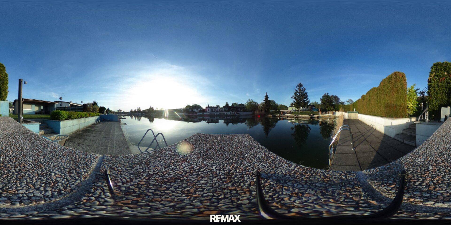 Panoramaansicht des Sees mit umliegenden Häusern, viel Grün und klarem Himmel.
