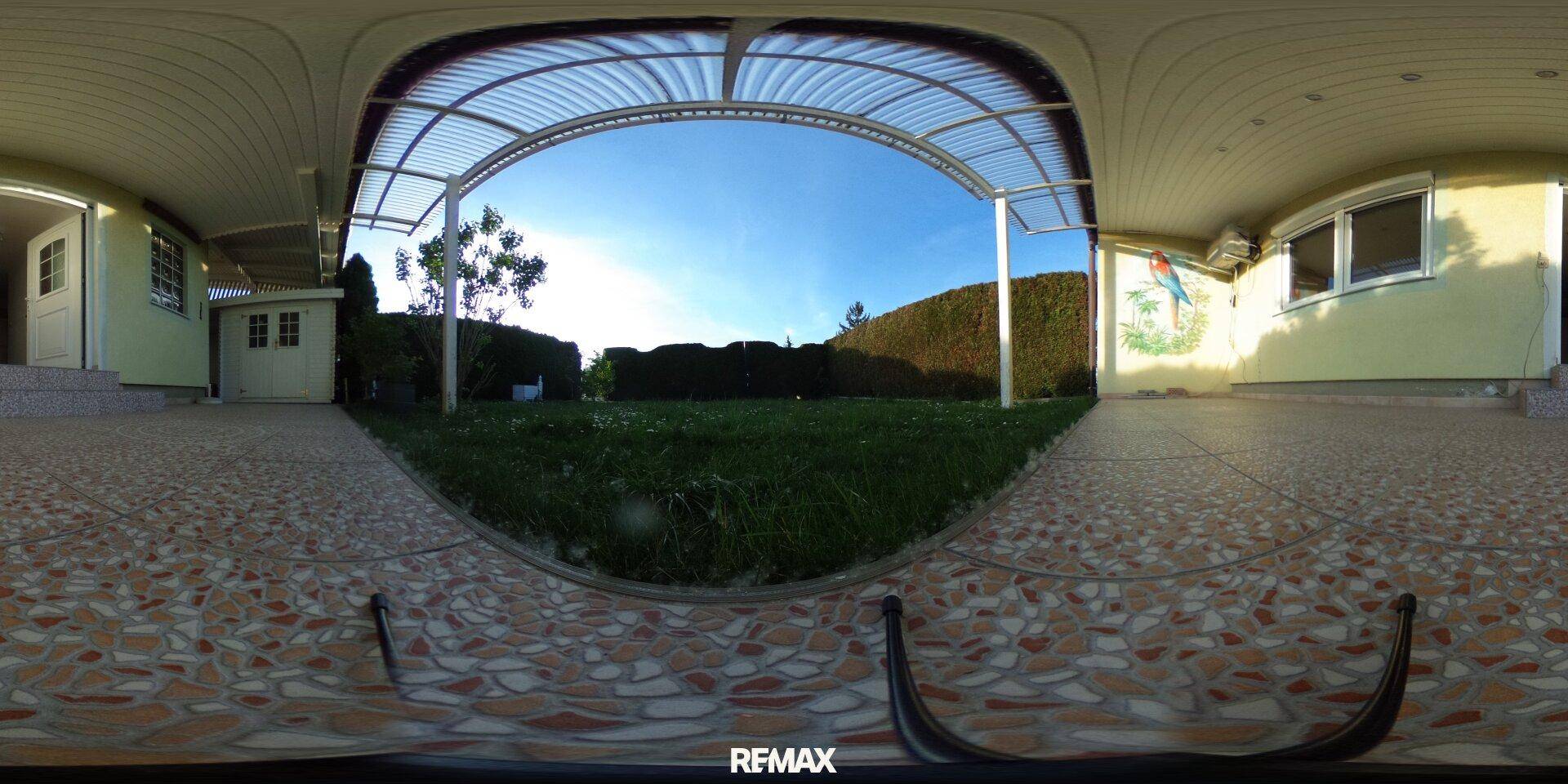 Panoramaansicht des Gartens mit Rasenfläche, gepflastertem Bereich und überdachter Terrasse.