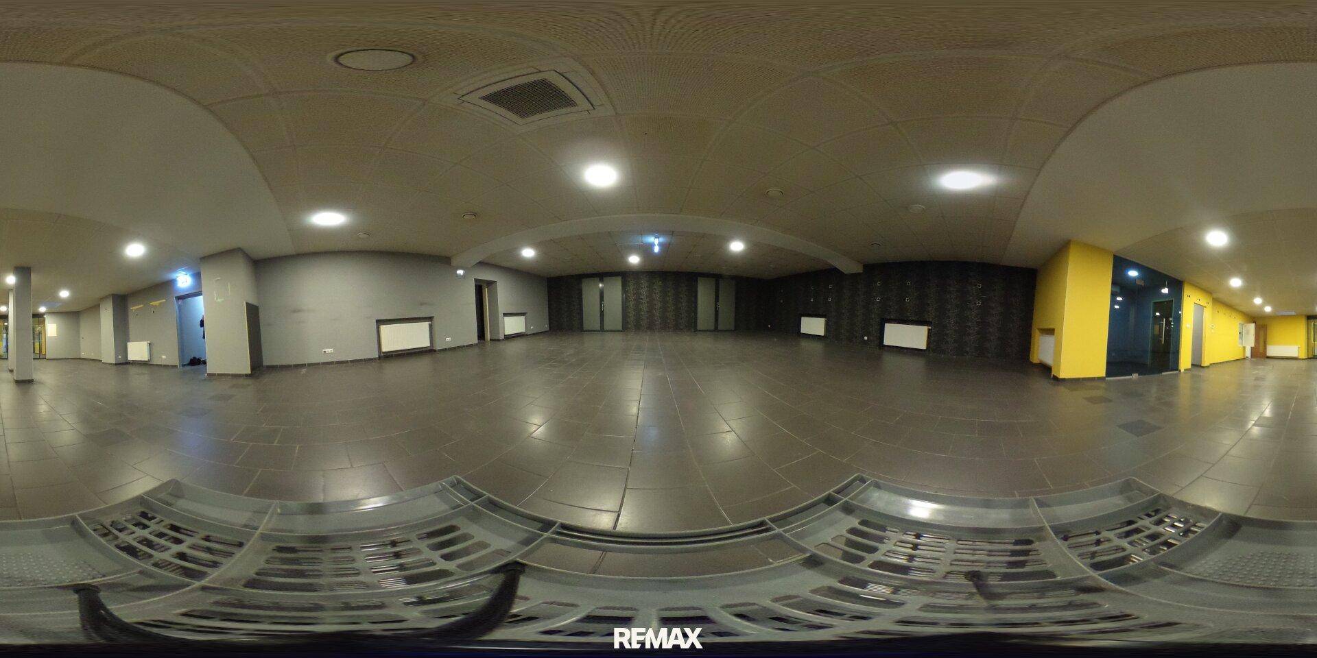Panoramaansicht eines weitläufigen Gewerberaums mit Fliesenboden, abgehängter Decke und farbigen Akzenten.
