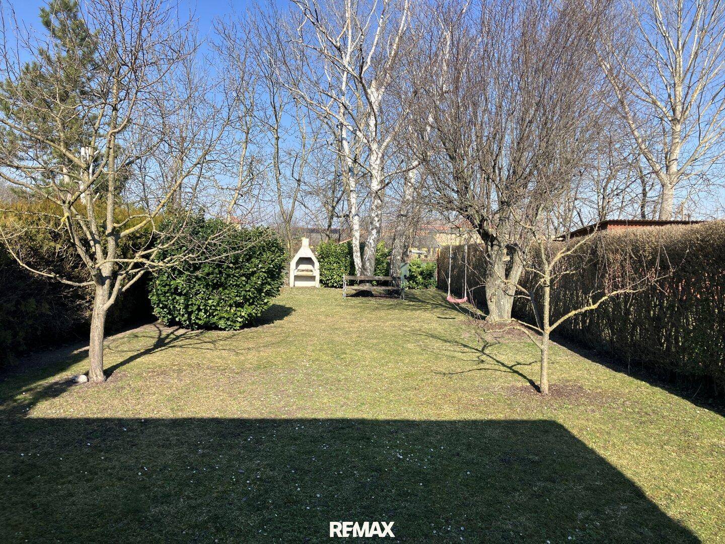 Großer Garten mit Rasenfläche, Bäumen und einem gemauerten Grill für gemütliche Stunden im Freien.