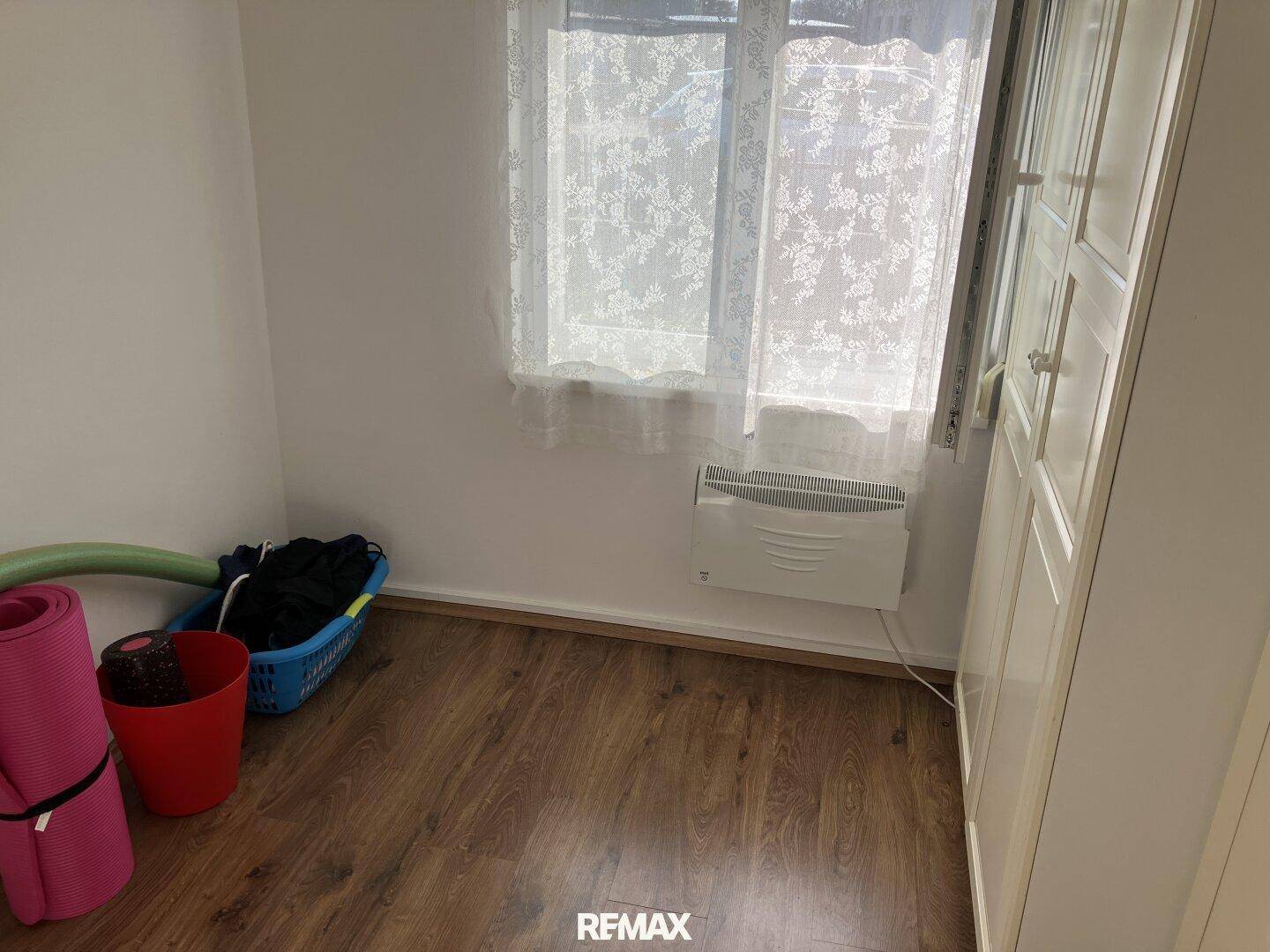 Kleines Zimmer mit Laminatboden, Fenster und einem Heizkörper, ideal als Schlaf- oder Gästezimmer.
