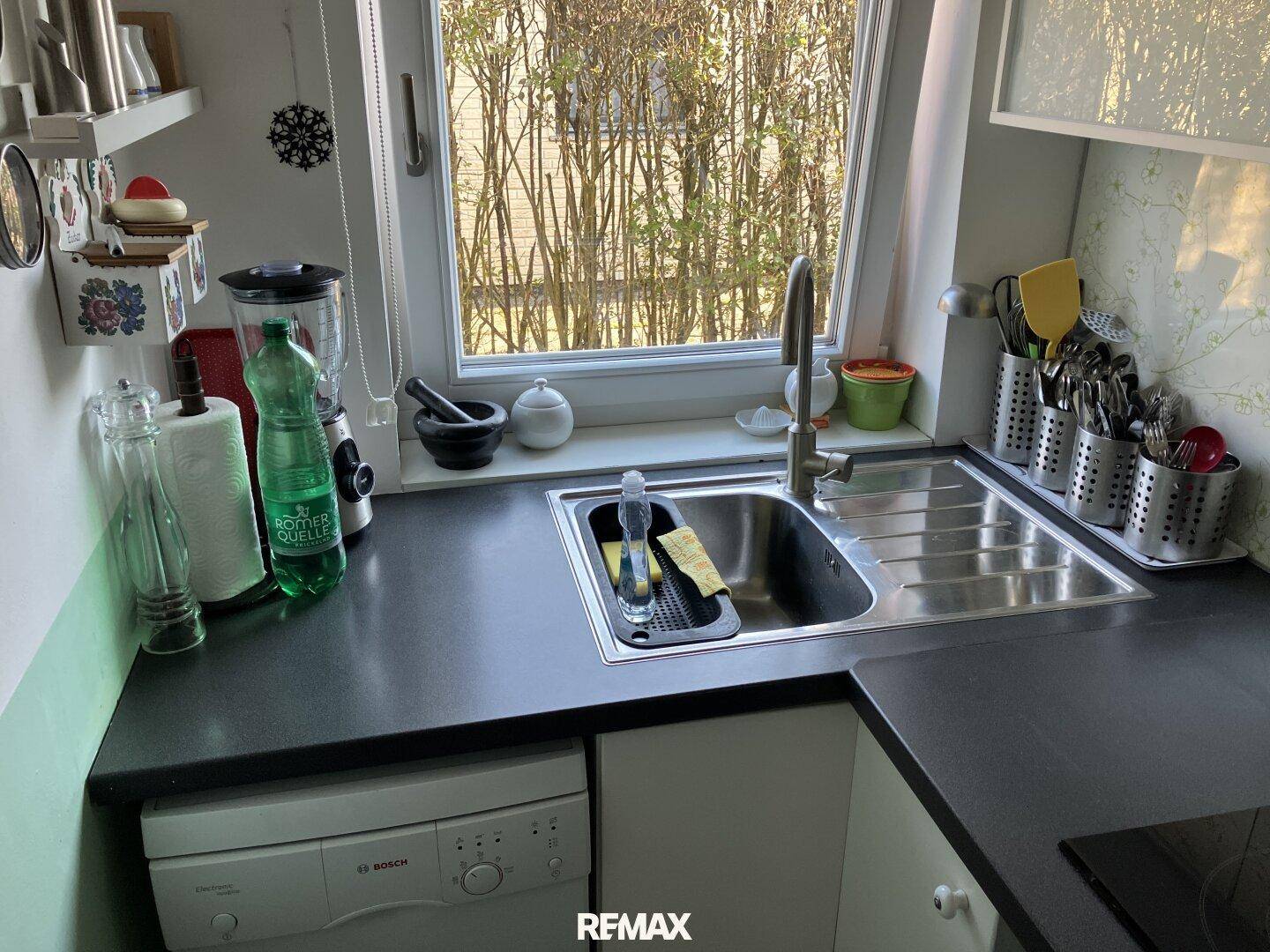 Helle Küche mit Spülbecken unter dem Fenster und integriertem Geschirrspüler.
