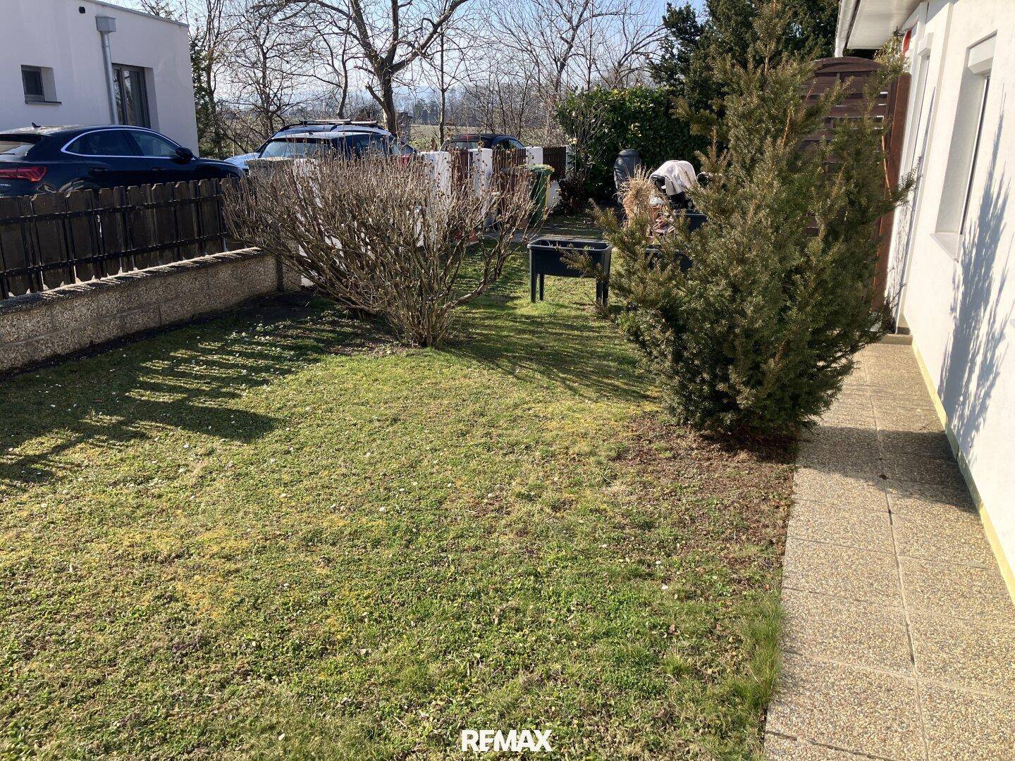 Kleiner, gepflegter Gartenbereich neben dem Haus mit Rasen und Sträuchern.