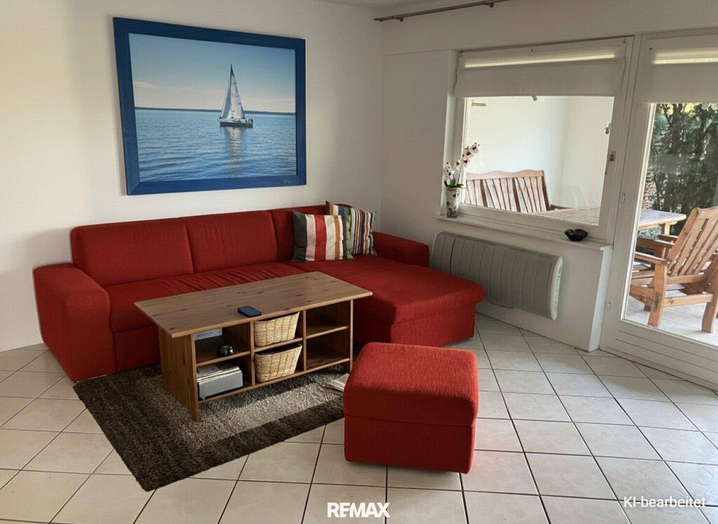 Gemütliches Wohnzimmer mit rotem Sofa, Couchtisch und Zugang zu einem Außenbereich.
