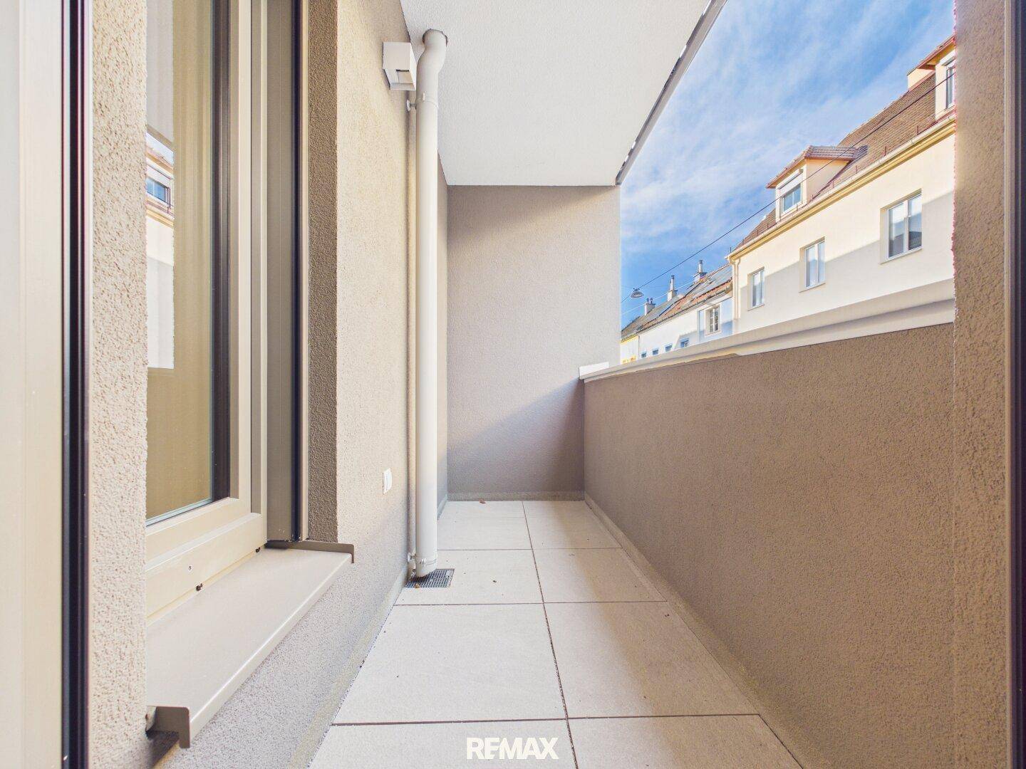 Schmaler Balkon mit Fliesenboden und Blick auf die umliegenden Gebäude einer städtischen Umgebung.