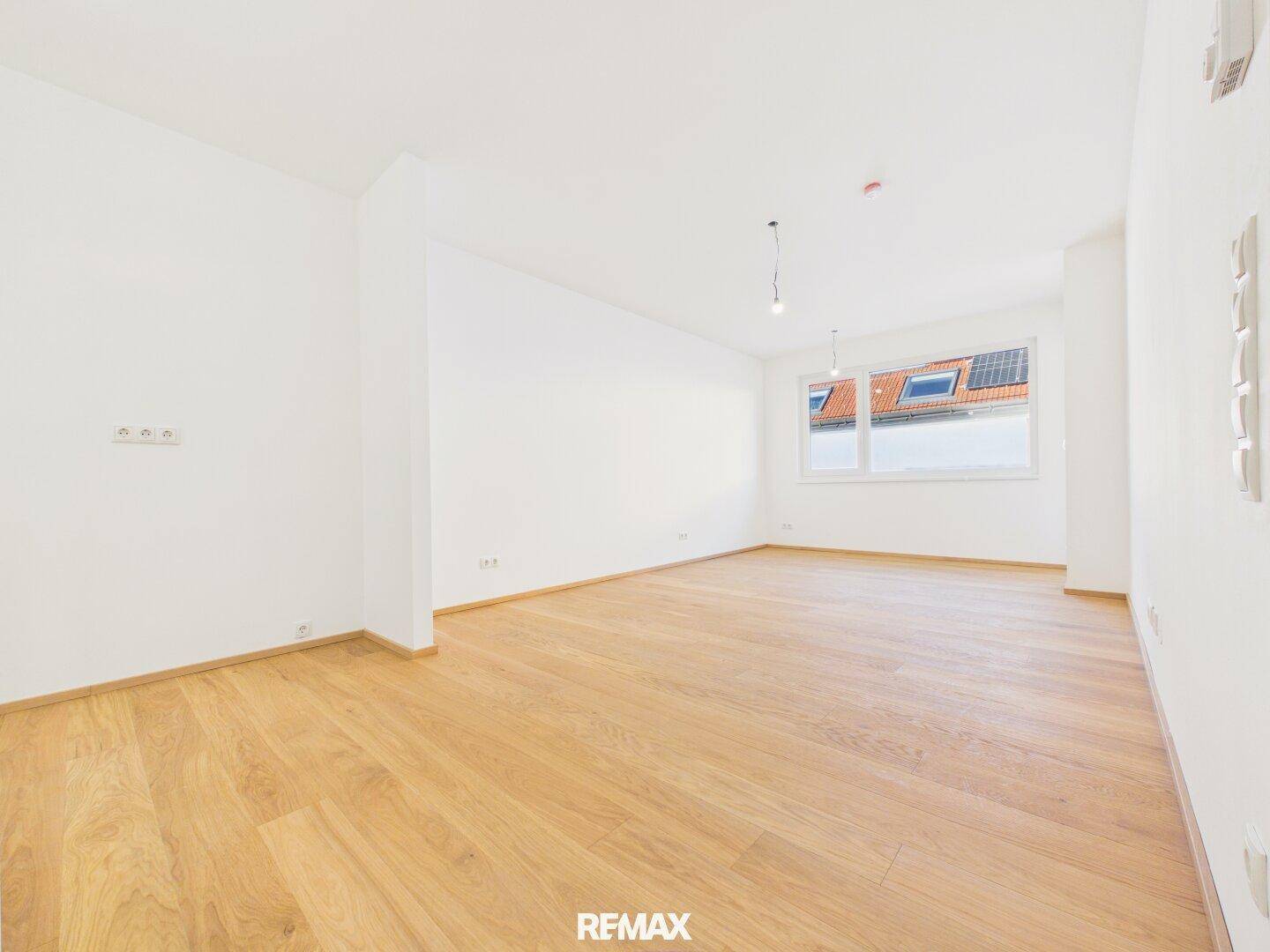Geräumiges, helles Zimmer mit Holzboden und Blick auf Dächer mit Solaranlagen.