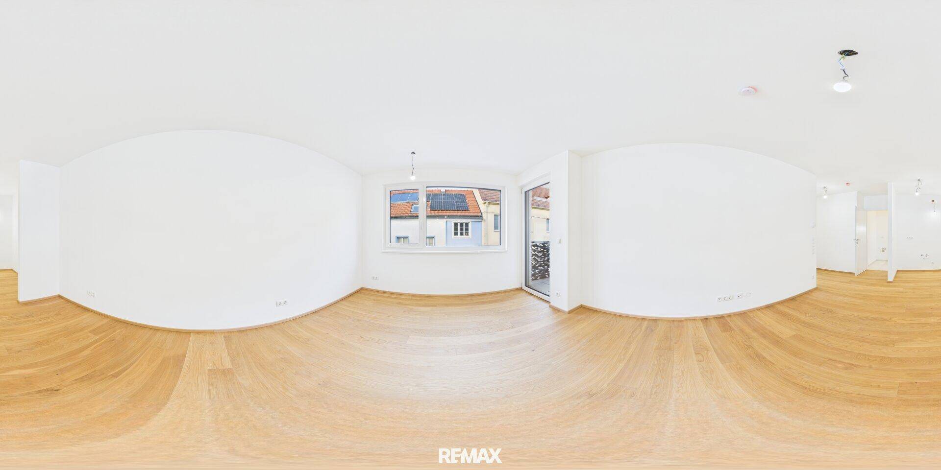 Weitläufiges, helles Wohnzimmer mit Holzboden und Zugang zum Balkon.