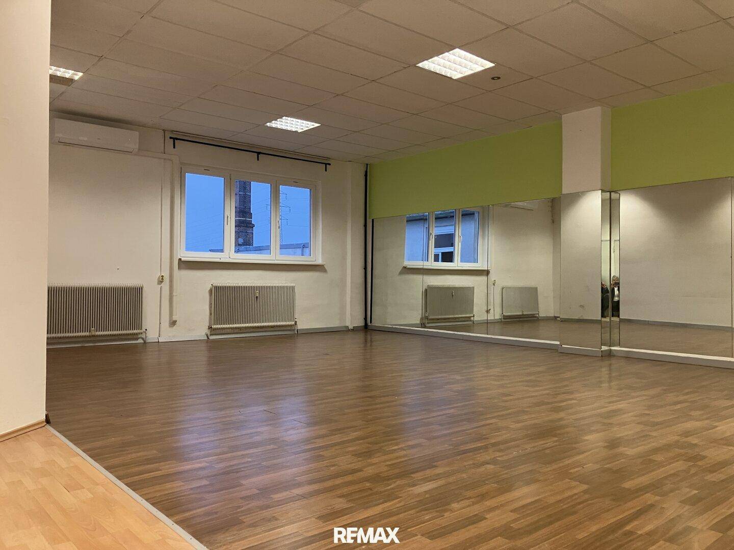 Leeres Tanzstudio mit hellem Holzfußboden, großen Wandspiegeln und Fenstern für natürliches Licht.