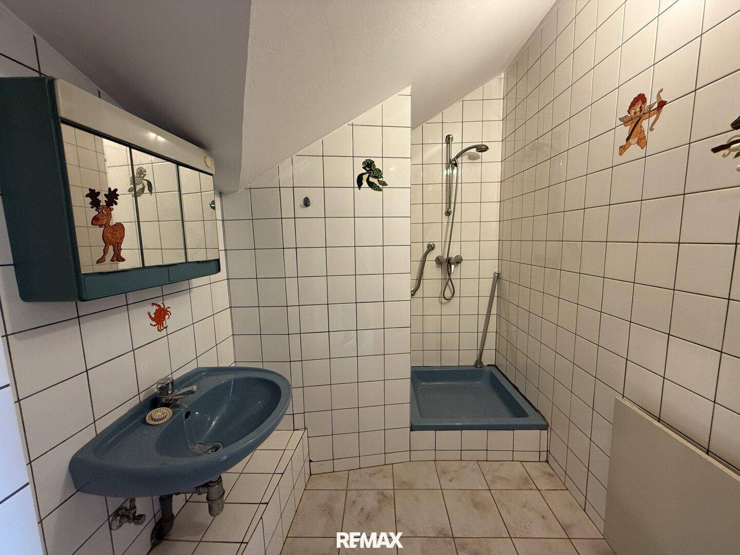 Badezimmer mit weißen Fliesen, blauer Keramik und Duschbereich, im Stil der 80er Jahre.