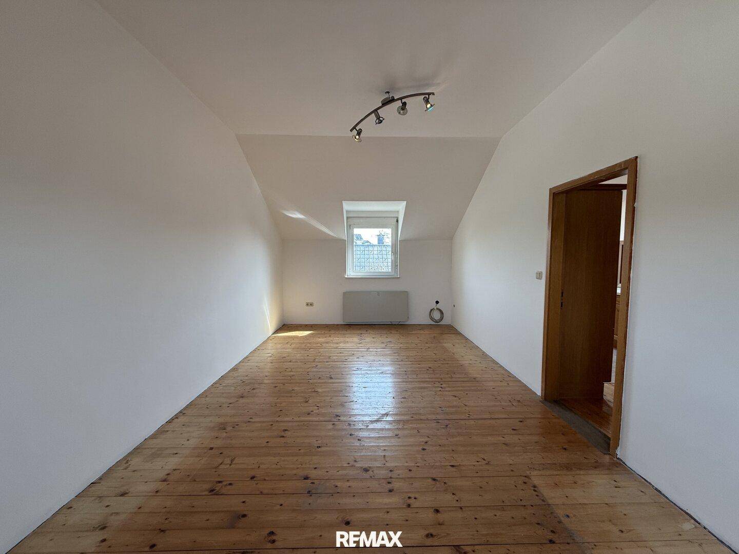 Helles Zimmer im Dachgeschoss mit Holzdielenboden und einem Dachfenster.