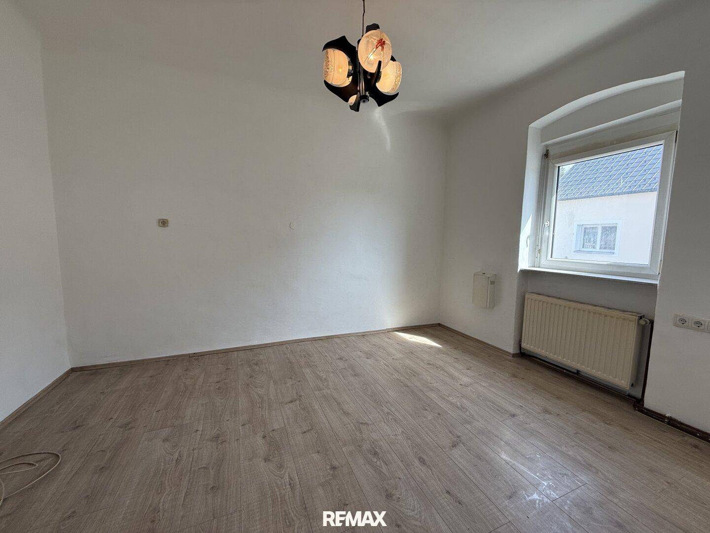 Einfaches, helles Zimmer mit Laminatboden und Fenster, bereit zur individuellen Gestaltung.
