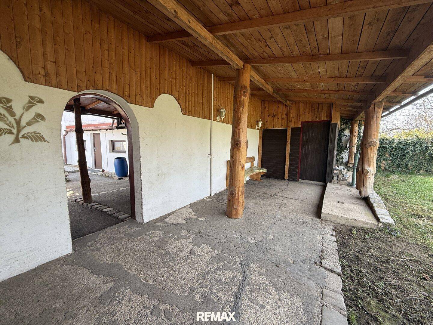 Überdachte Terrasse mit Holzbalken und rustikalem Charme, angrenzend an einen Gartenbereich.