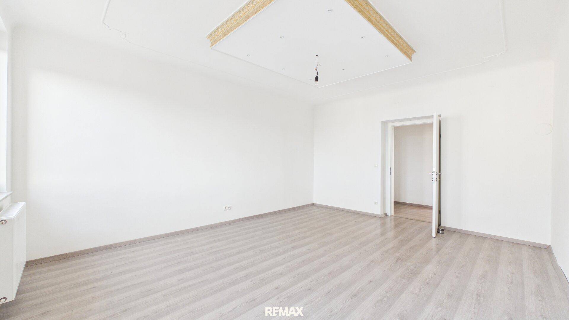 Leeres, helles Zimmer mit Laminatboden, weiß gestrichenen Wänden und einer offenen Tür.