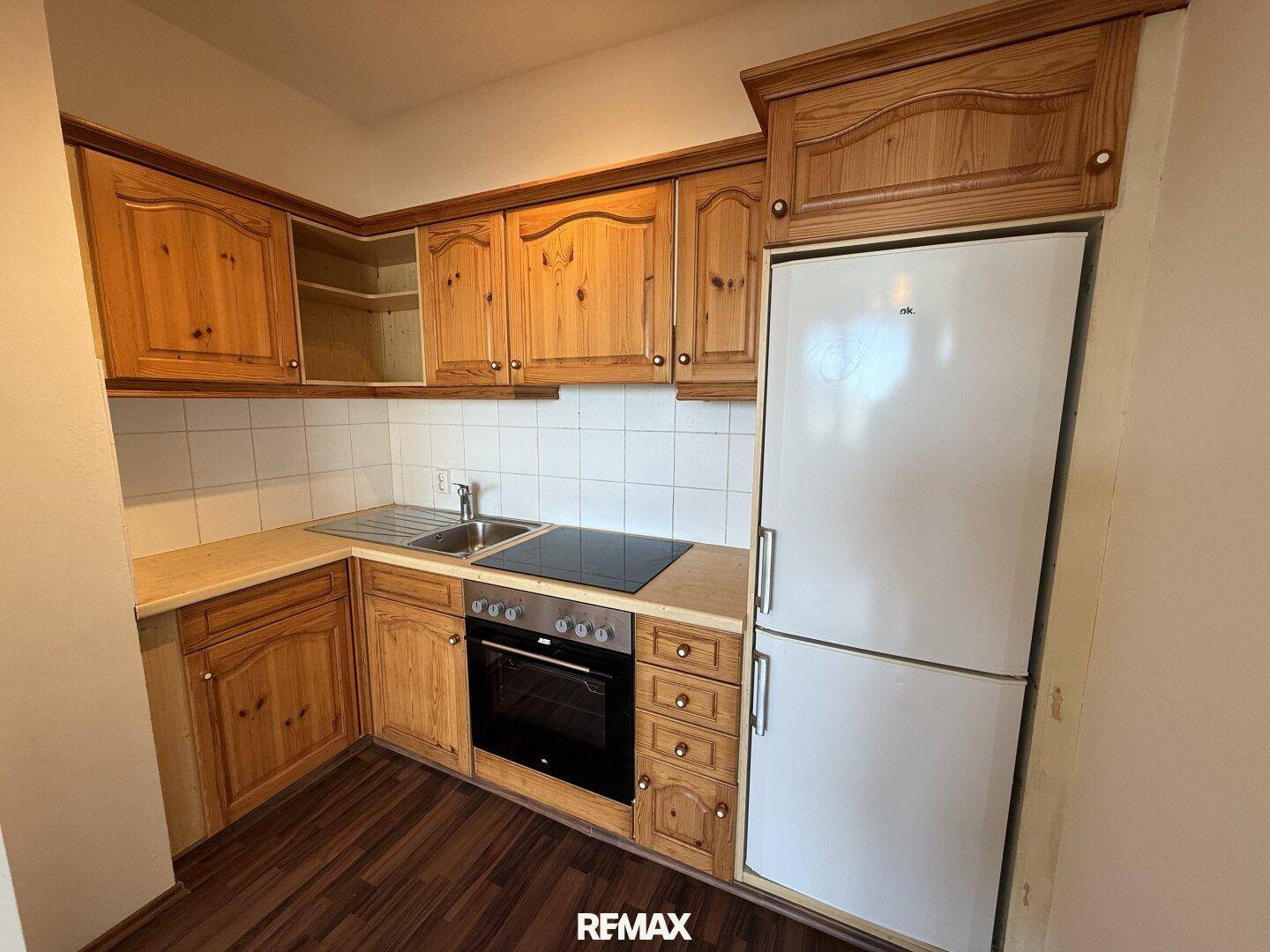 Funktionale Küchenzeile mit Holzschränken, Elektroherd und Kühlschrank in einem kompakten Raum.