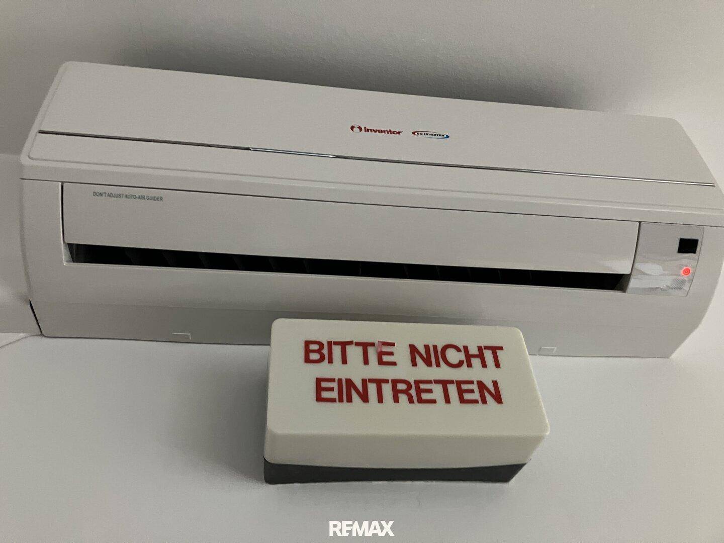 Eine weiße Klimaanlage ist an der Wand montiert, davor steht ein Schild mit der Aufschrift 'Bitte nicht eintreten'.