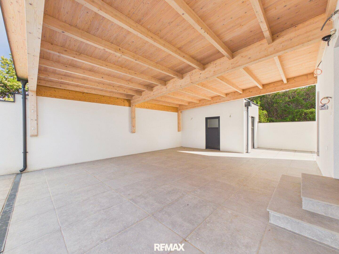 Überdachter Außenbereich mit Holzbalken und gefliestem Boden, ideal als Carport oder Lagerfläche.